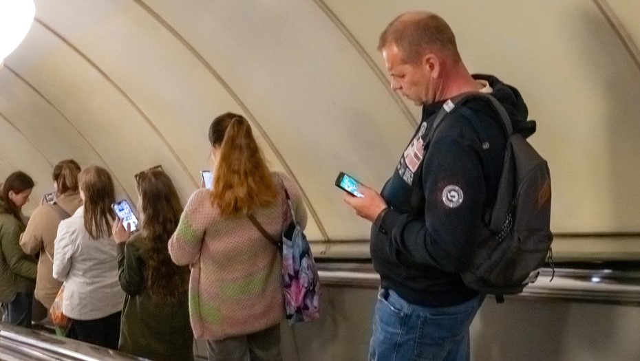 Подземный интернет. Группа пассажиров метро спускается на эскалаторе и просматривает сообщения на экране смартфона.