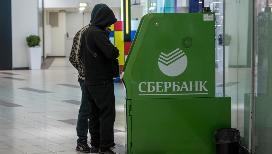 Мужчины стоят у банкомата Сбербанка.