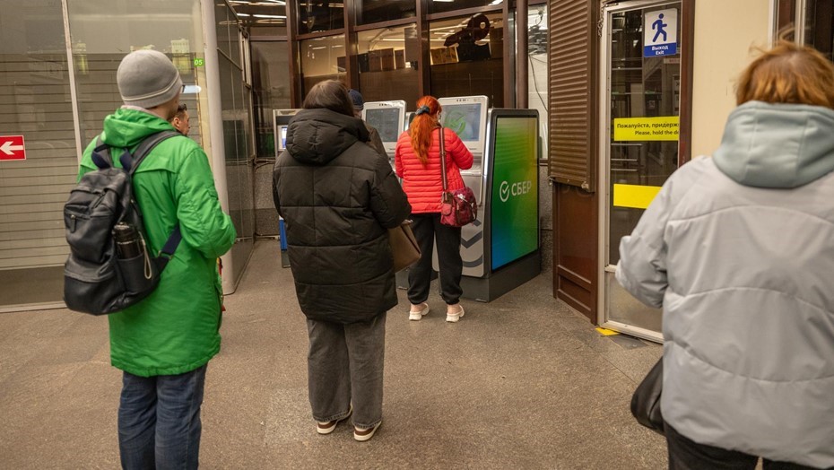 Люди стоят в очереди к банкомату для получения наличных