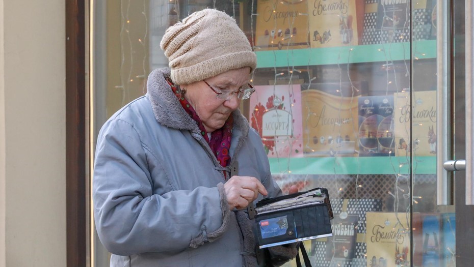 Россия, Санкт-Петербург. Пенсионерка с кошельком на фоне витрины магазина. 